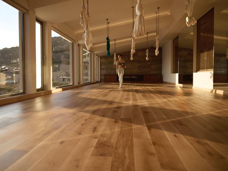 Světlá prázdná místnost s dřevěnou podlahou a velkými okny s výhledem na hory v hotelu.