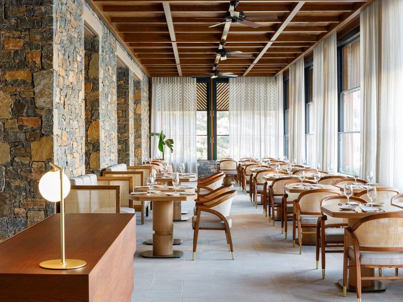 Světla moderní hotelová restaurace s dřevěnými židlemi, stoly a velkými okny.