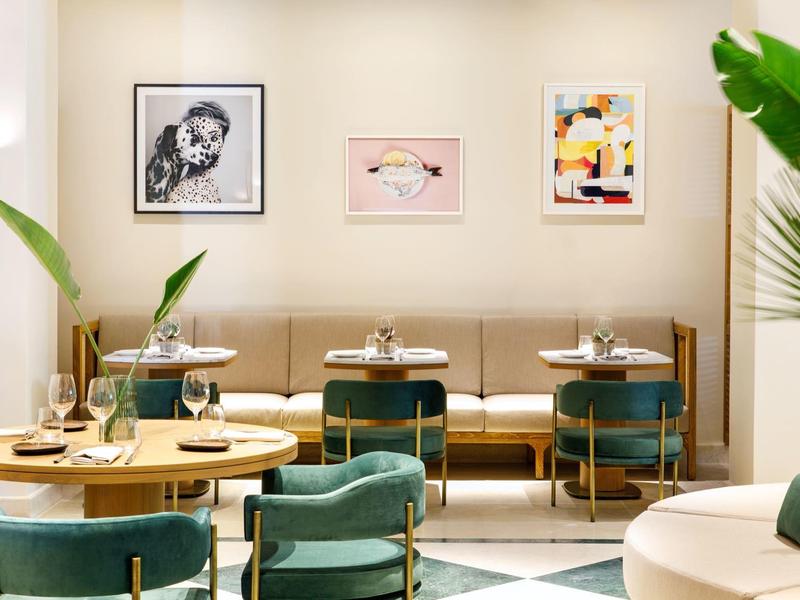 Moderní restaurace se zelenými židlemi, dřevěnými stoly a uměním na stěnách.