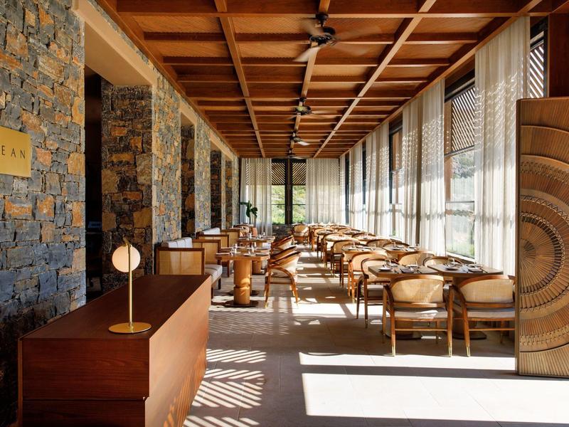 Světlý hotelový lounge s kamennými zdmi, dřevěným nábytkem a velkými okny