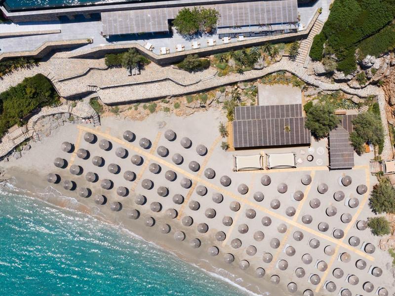 Letecký pohled na pláž s deštníky vedle hotelového bazénu a baru.