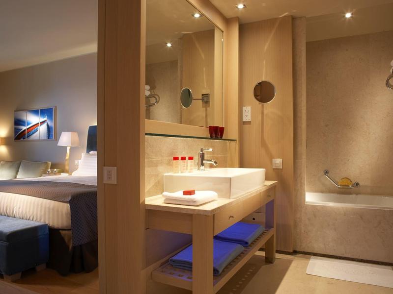 Moderní hotelová koupelna s umyvadlem a vanou, sousedící s ložnicí.