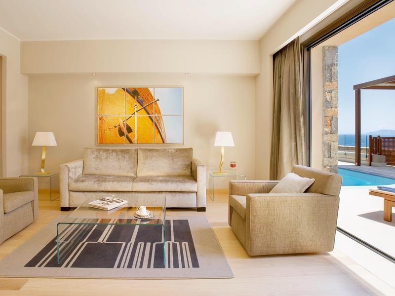 Moderní obývací pokoj s pohovkou, křeslem a přístupem na terasu s bazénem a výhledem na moře.