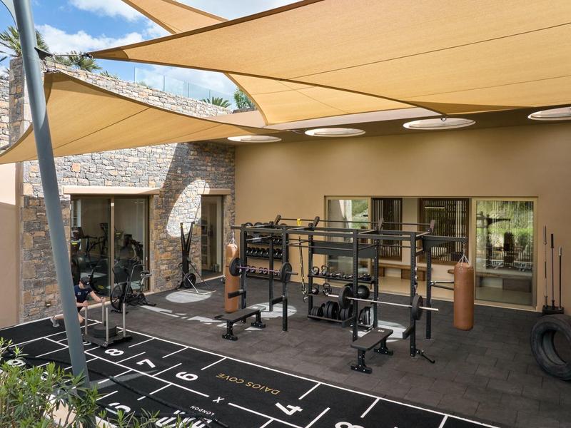 Moderní venkovní fitness prostor s ochranou proti slunci a různým tréninkovým vybavením.