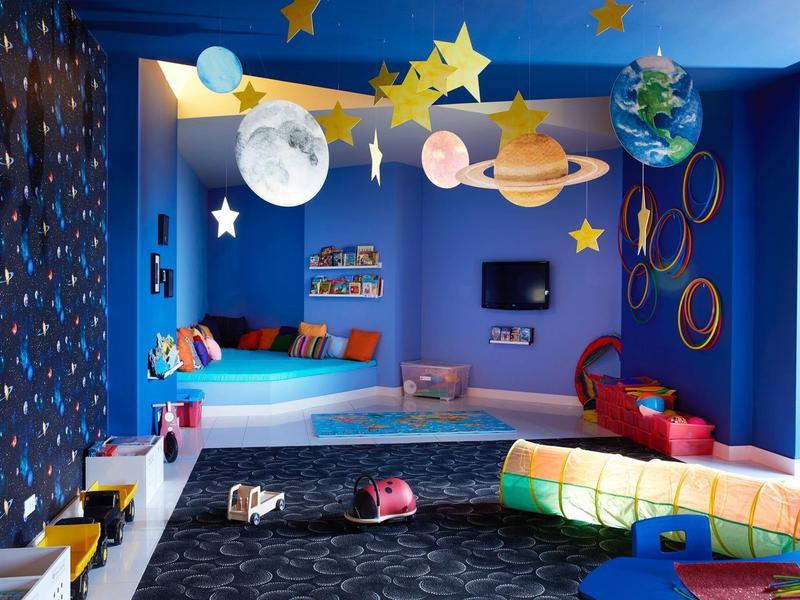 Barevná dětská herna s planetárním mobilem a útulným posezením.