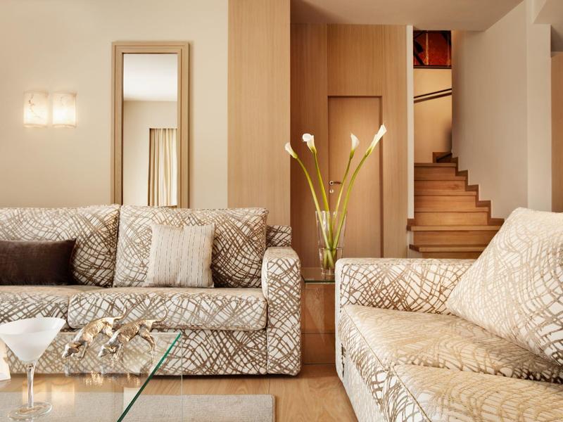 Elegantní hotelový pokoj s vzorovanými pohovkami, skleněným konferenčním stolkem a schody v pozadí.