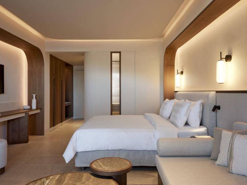 Moderní hotelový pokoj s velkou postelí, pohovkou a teplým osvětlením.