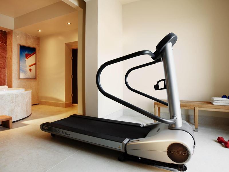 Moderní běžecký pás v světlé, prostorné posilovně s ručníky a činkami.