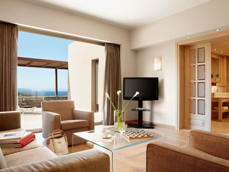 Moderní hotelový pokoj s velkou postelí a výhledem na terasu a moře.