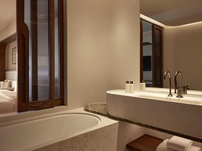 Moderní koupelna s vanou a umyvadlem vedle otevřeného okna do ložnice.