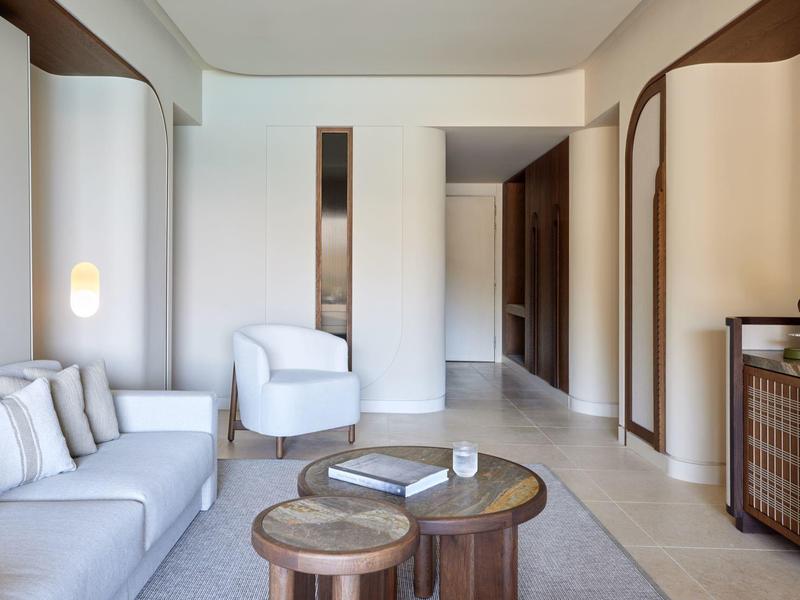 Světý a moderní obývací pokoj s pohovkou, křesly a kulatým dřevěným stolem v hotelovém pokoji.