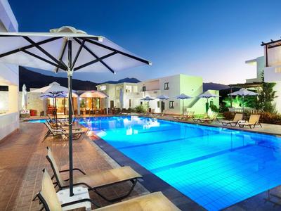 Großer Pool bei Sonnenuntergang mit weißen Liegen, Schirmen und modernen weißen Gebäuden.