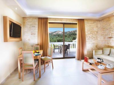 Helles Wohnzimmer mit Steinwand, Sofa, Holztisch, Esstisch, TV und Blick auf Terrasse und grüne Hügel.
