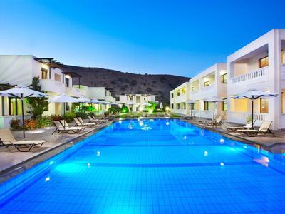 Moderner Hotelpool bei Dämmerung, umgeben von weißen Gebäuden und Sonnenschirmen.