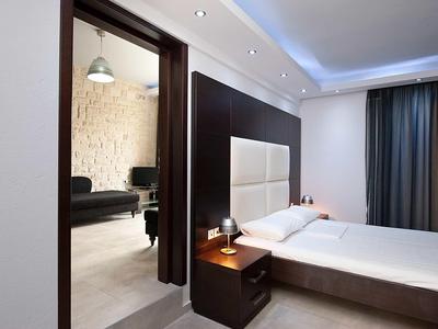 Modernes Schlafzimmer mit großem Bett, dunklem Holz, weißen Wänden und Blick in angrenzendes Zimmer.