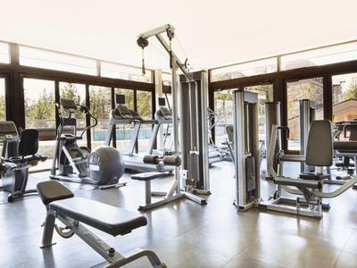 Helles Fitnessstudio mit Kraft- und Ausdauergeräten vor großen Fenstern und Blick ins Freie.