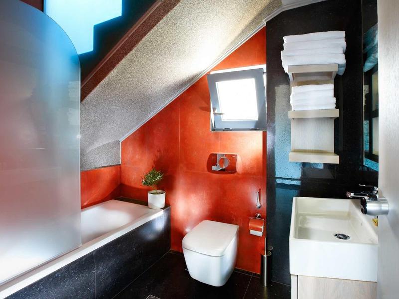 Modern badkamer onder schuine plafond met rode muur, bad, toilet en wastafel.