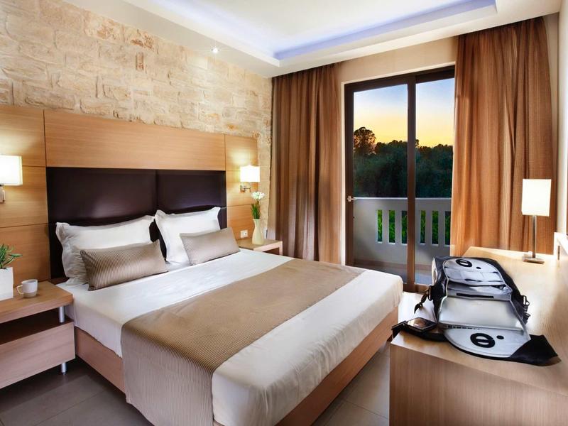 Gezellige hotelkamer met tweepersoonsbed, warme houttinten en balkonzicht bij zonsondergang.