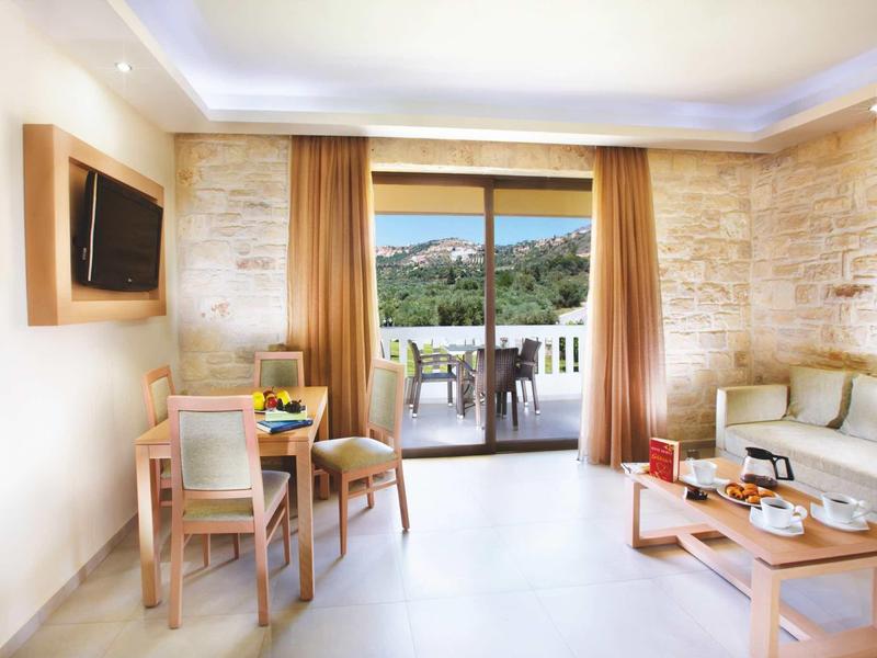 Lichte woonkamer met stenen muur, ronde eethoek en balkon met uitzicht op de bergen.