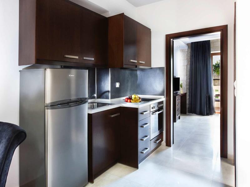 Moderne kleine keuken met donkere kasten, roestvrijstalen apparaten en lichte muren in een hotelkamer.