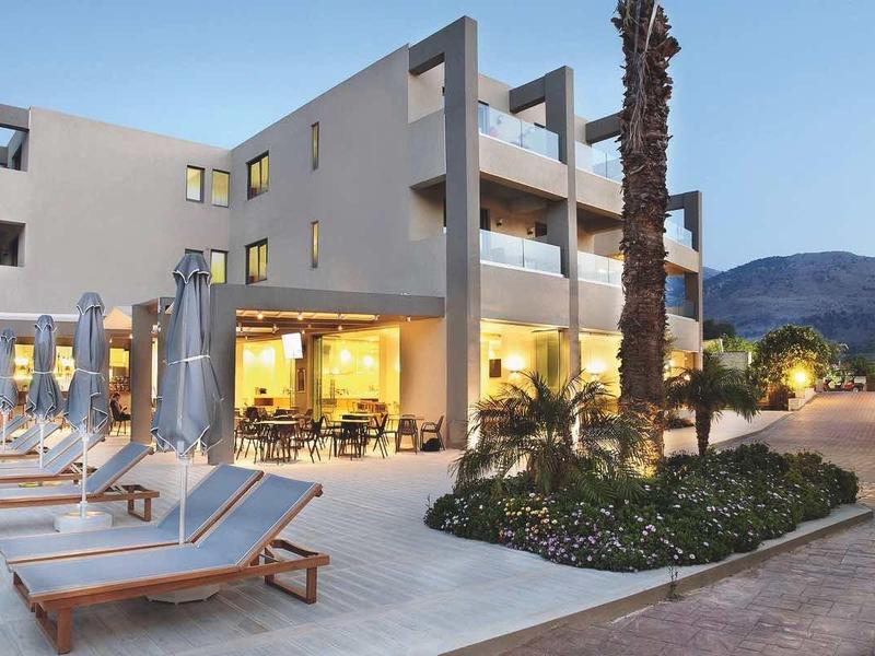 Modern hotel met zwembad, ligstoelen en verlichte zwembadzone bij schemering.