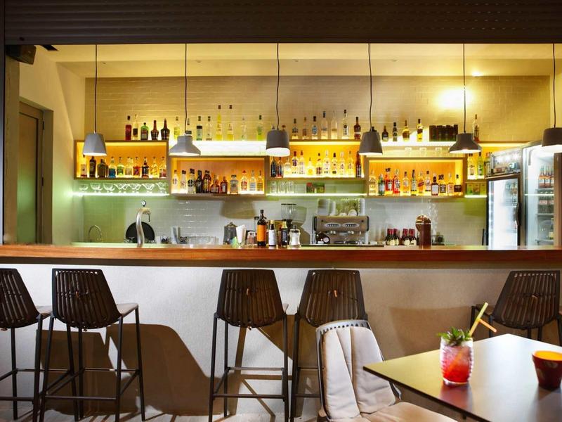 Moderne hotelbar met verlichte planken, vier barkrukken en een tafel met drankjes.