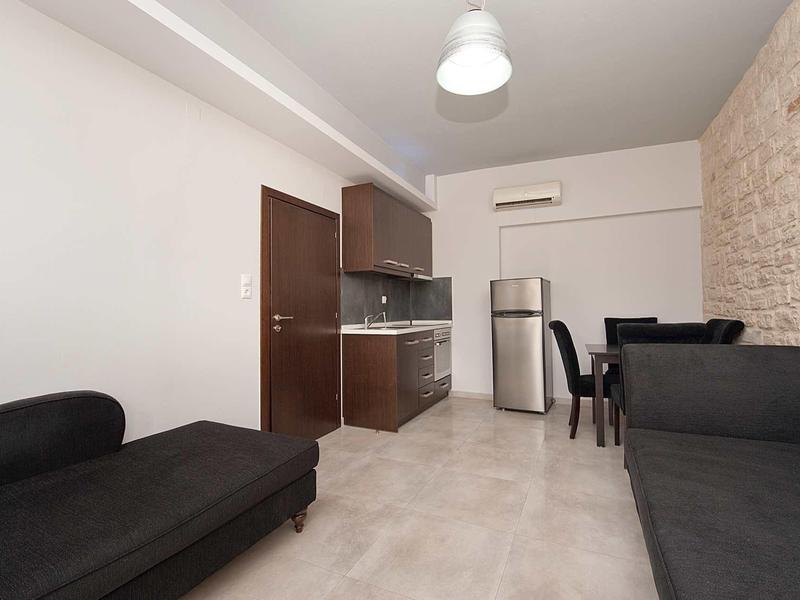 Kleine moderne woonkamer met kitchenette, zwarte bank en eetgedeelte.