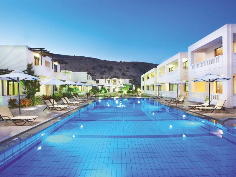 Hotel met groot verlicht zwembad en ligstoelen bij zonsondergang.