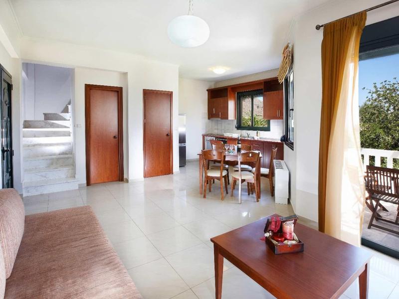 Lichte woonkamer met bruine bank, eettafel en toegang tot een balkon met uitzicht op groen.