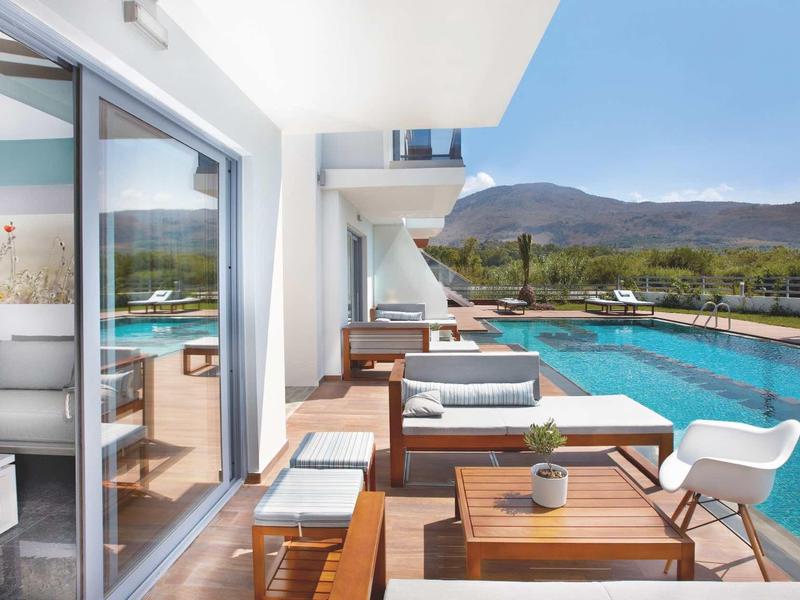 Modern hotelkamer met terras en uitzicht op een zwembad en berglandschap.