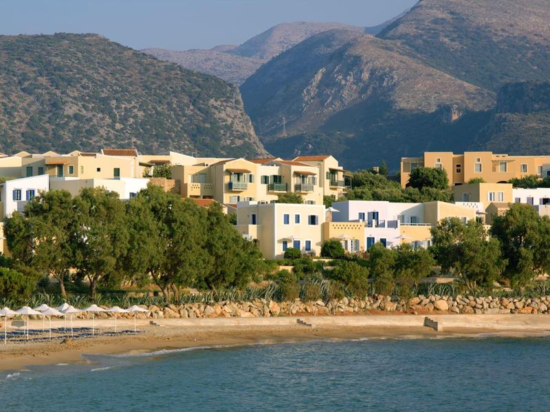 Complejo hotelero en la playa con montañas al fondo bajo cielo despejado.