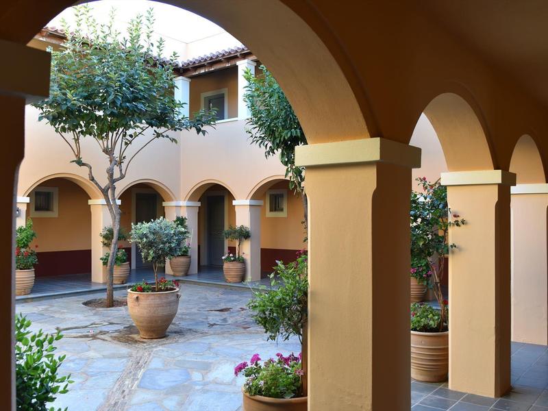 Patio interior de hotel con arcos de piedra, plantas en macetas y árboles pequeños