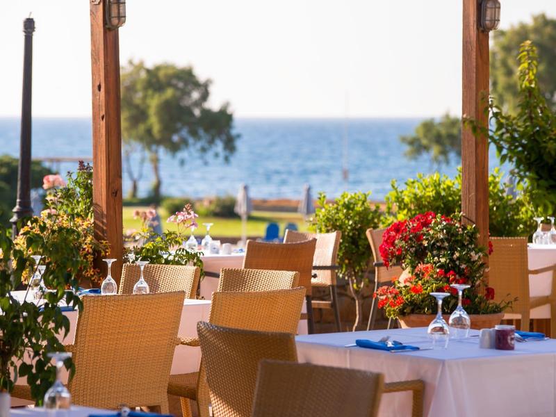 Terraza de restaurante con mesas puestas y vista al mar en un día soleado.