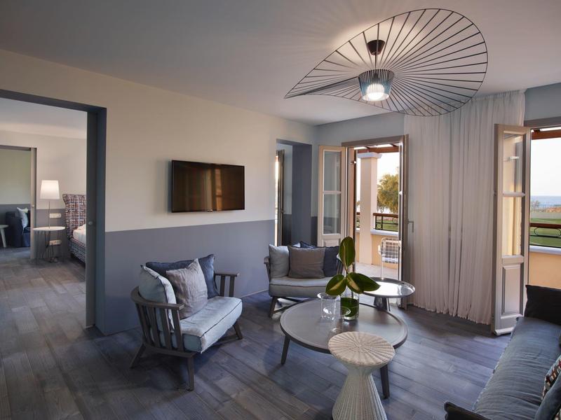 Sala moderna con sillones, mesa de centro y vista a la terraza y el mar a través de puertas abiertas.