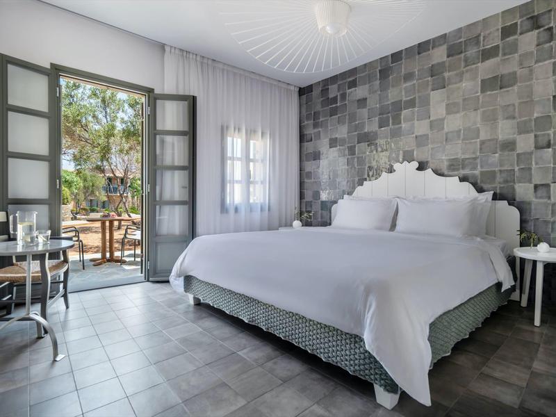 Habitación de hotel moderna con cama doble, pared de acento gris y acceso a terraza con sillas.