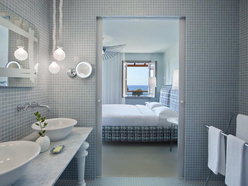 Baño moderno de hotel con lavabo y vista a una habitación y al mar.