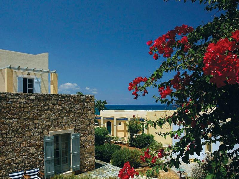 Patio del hotel con flores rojas, arbustos y edificio de piedra bajo un cielo azul claro.
