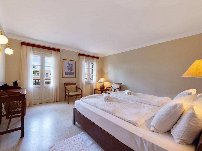 Habitación de hotel luminosa con cama doble, sillas, escritorio y balcón con luz natural.