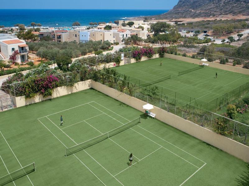 Vista de canchas de tenis y césped con casas de vacaciones y mar al fondo.