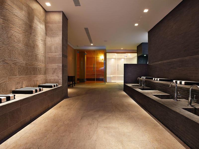 Área de lavado moderna en hotel con múltiples lavabos y revestimientos de madera y piedra.