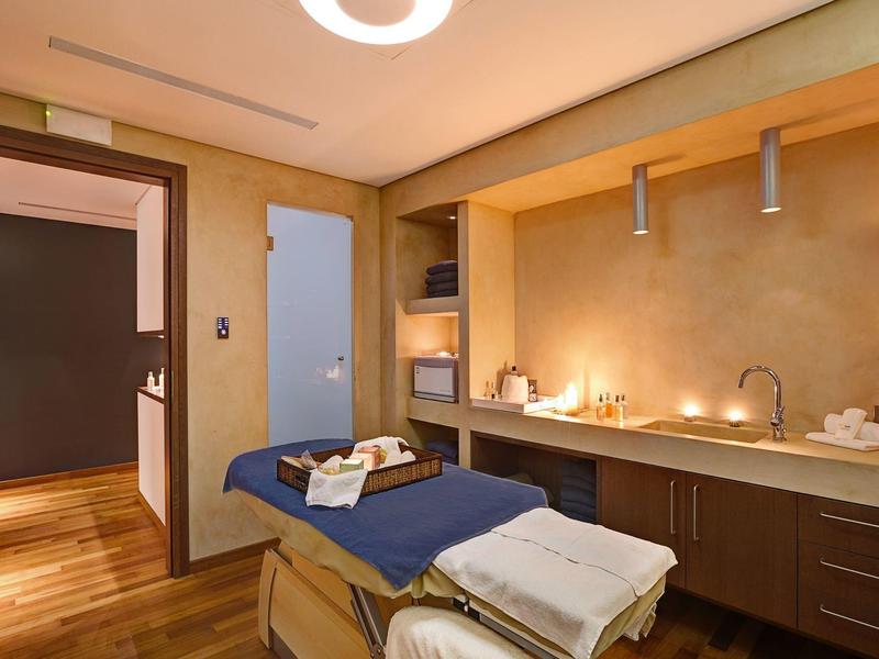 Acogedora sala de spa con camilla de masaje, iluminación suave y piso de madera.