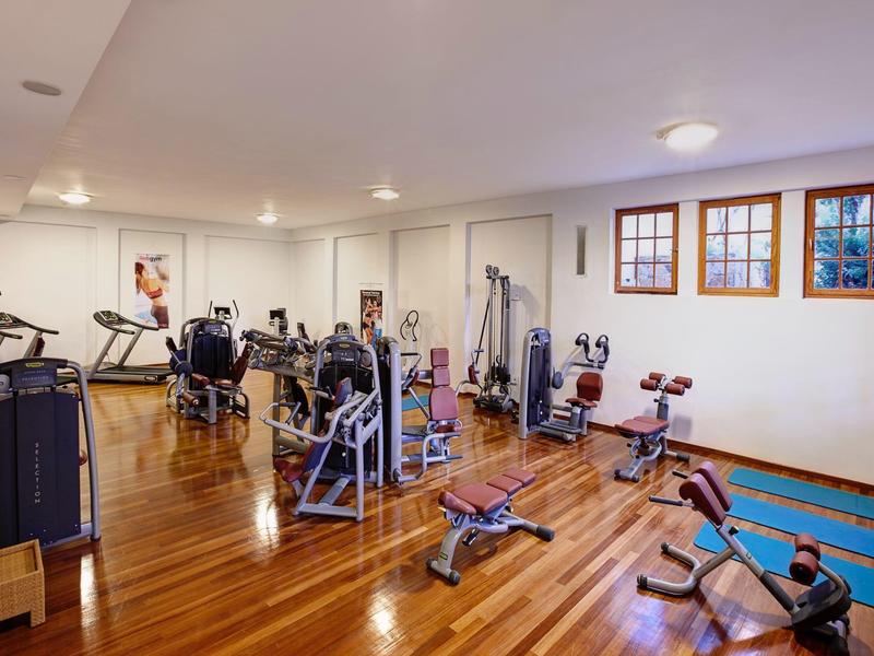Gimnasio con máquinas de ejercicio y equipo en un piso de madera con ventanas.