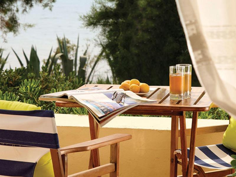 Mesa con periódico, jugo y limones en una terraza con sillas y plantas alrededor