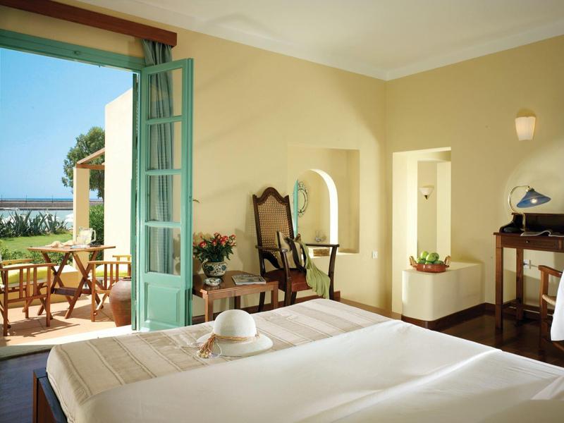 Habitación de hotel luminosa con balcón abierto, dos camas y vista a la terraza y al mar.