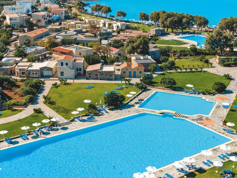 Gran complejo con varias piscinas, tumbonas y edificios mediterráneos junto al mar.