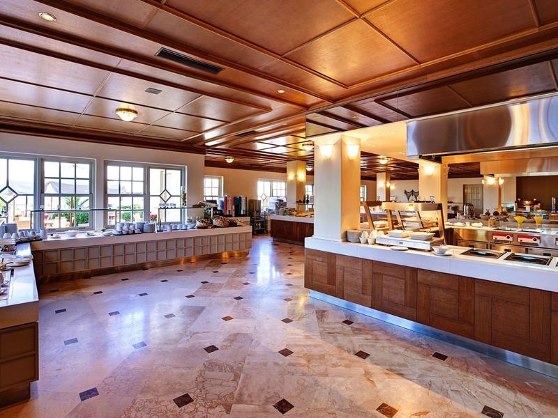 Amplia zona de buffet en hotel con detalles de madera, suelo de mármol y grandes ventanales.