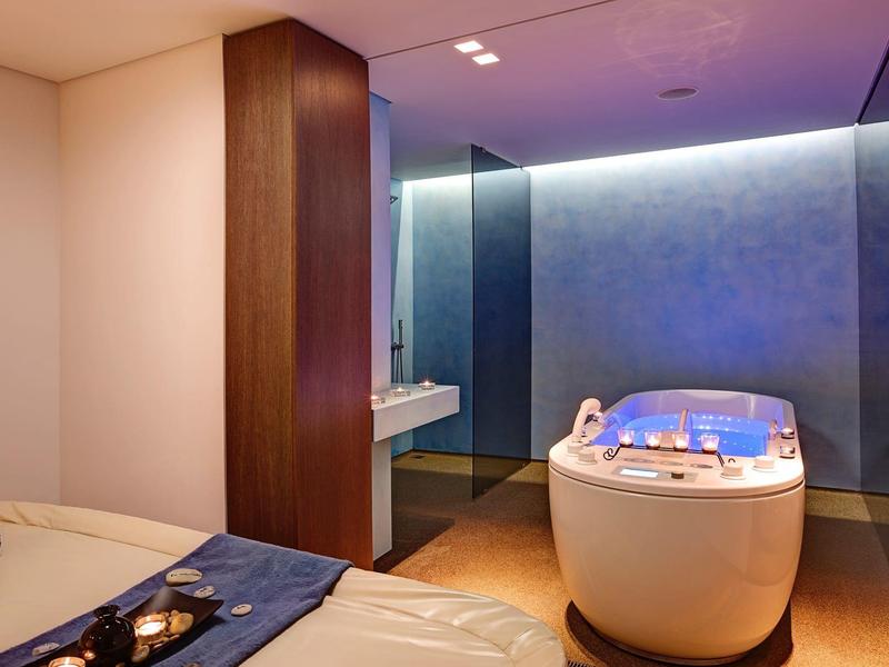 Área de spa moderna con jacuzzi, camilla de masaje y iluminación relajante en tonos cálidos.