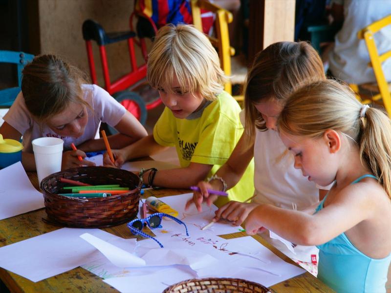 Cuatro niños sentados en una mesa, pintando juntos sobre hojas de papel blancas.