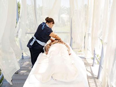 Masaż na zewnątrz na stole z białymi zasłonami i światłem naturalnym.