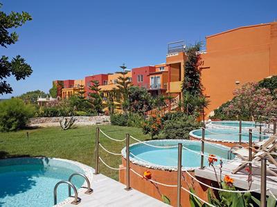 Kompleks hotelowy z okrągłymi basenami otoczonymi zielenią i wielopiętrowymi budynkami pod jasnym niebem.